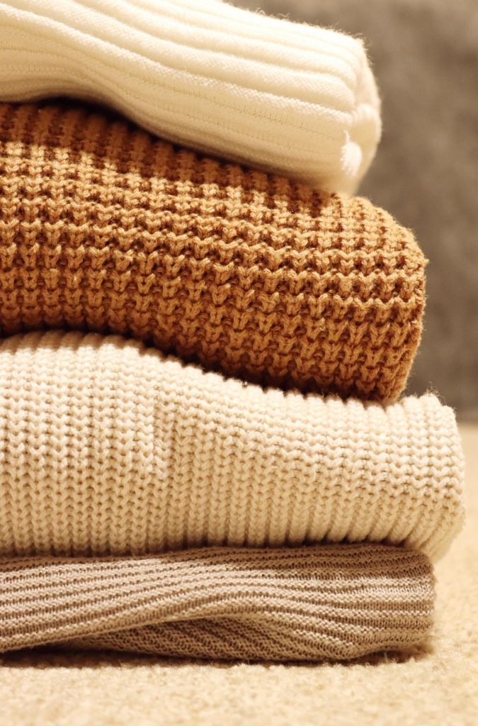 A pile of beige and white sweaters. 
